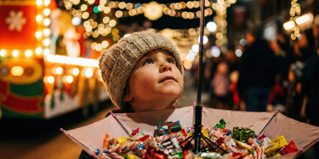Niño mirando las luces navideñas mientras sostiene un paraguas lleno de caramelos en una cabalgata.