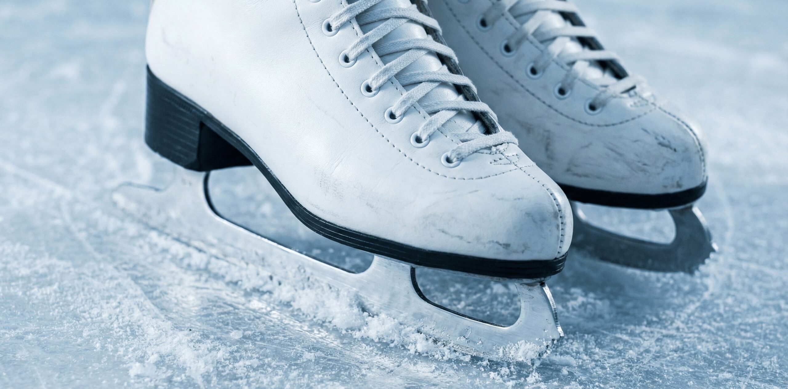 Primer plano de unos patines de hielo blancos sobre una pista con hielo rasgado.