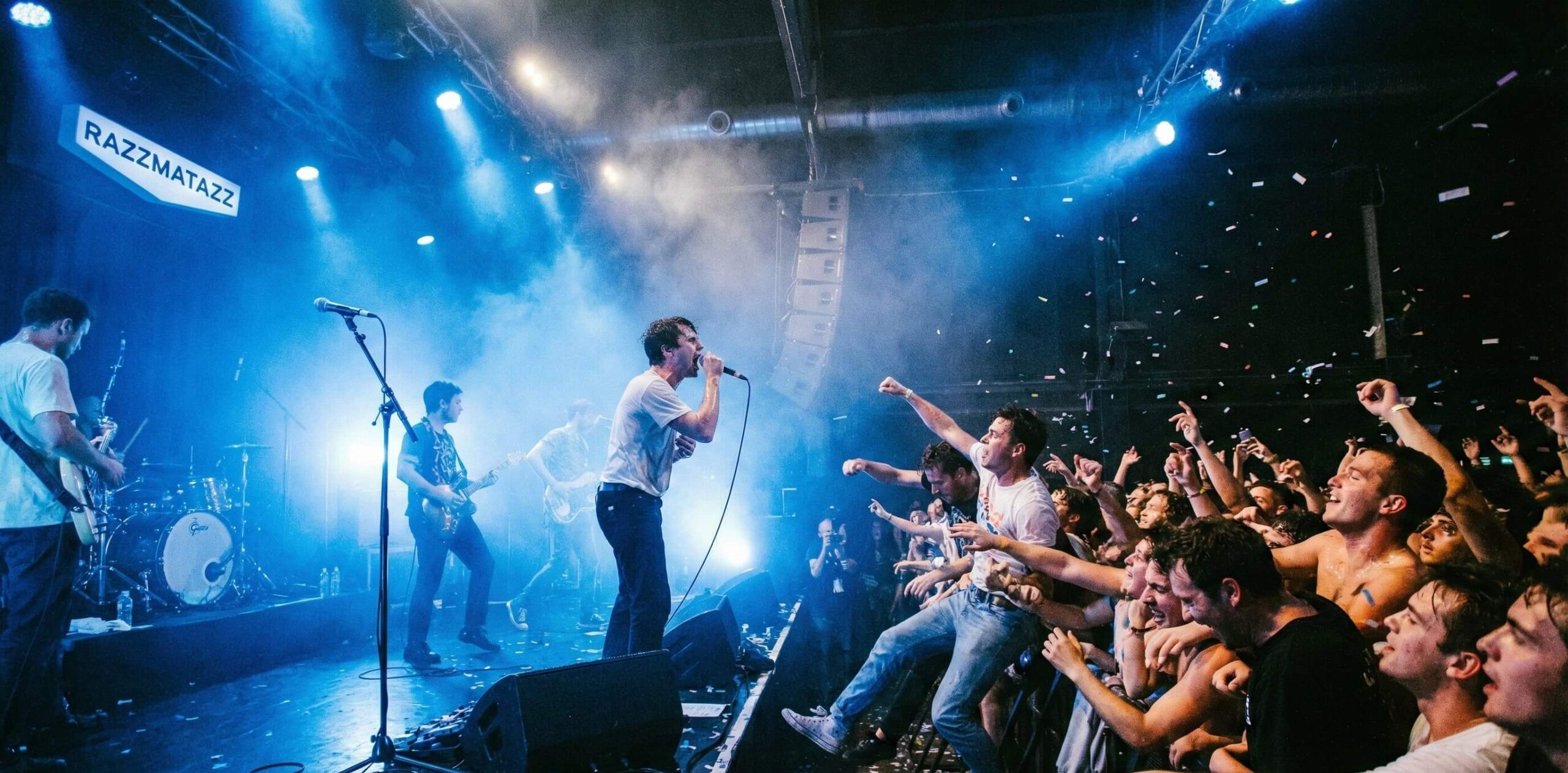 Concierto de banda en vivo en la sala Razzmatazz con confeti y luces azules.