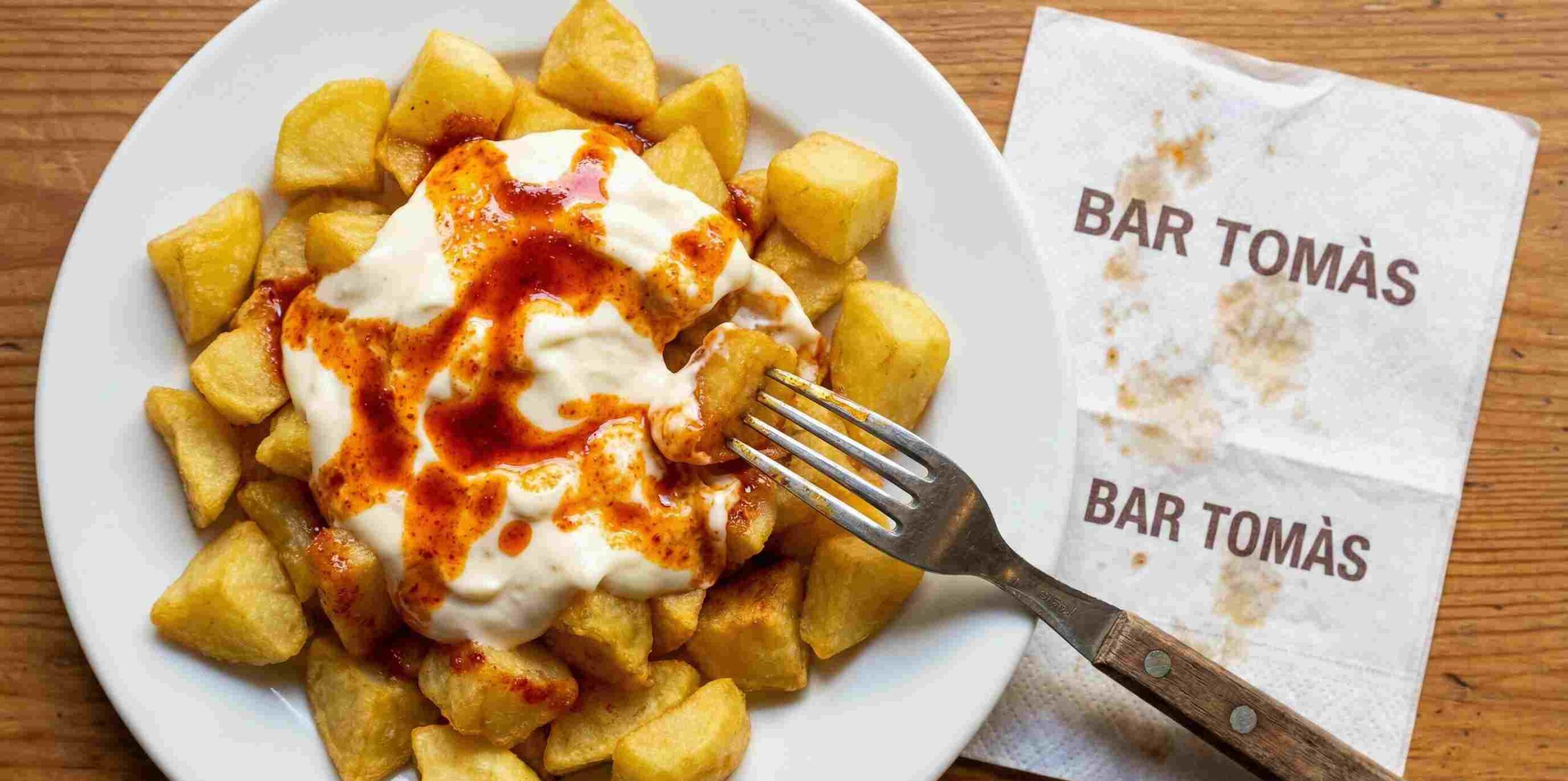 Ración de las famosas patatas bravas del Bar Tomàs de Sarrià con servilleta del local.